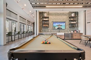 A pool table is in the middle of a room with a brick wall and a picture of a beach house.